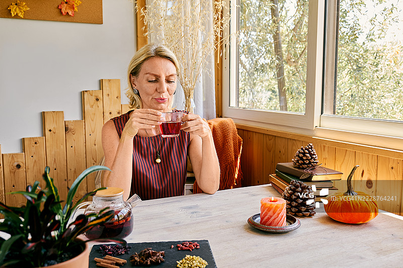 金发成熟的女性在家中用玻璃茶杯喝洛神花茶图片素材