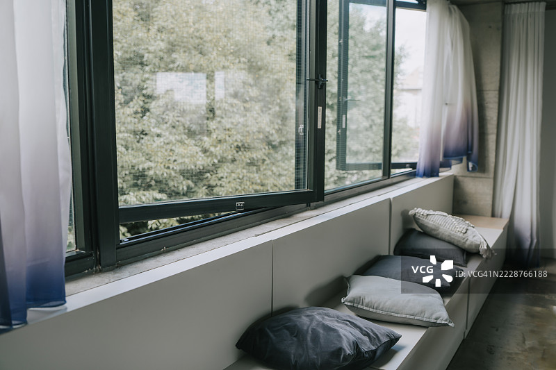 现代简约风格的窗边座椅，配有靠垫和明亮的开放窗户，营造出宽敞的生活空间图片素材