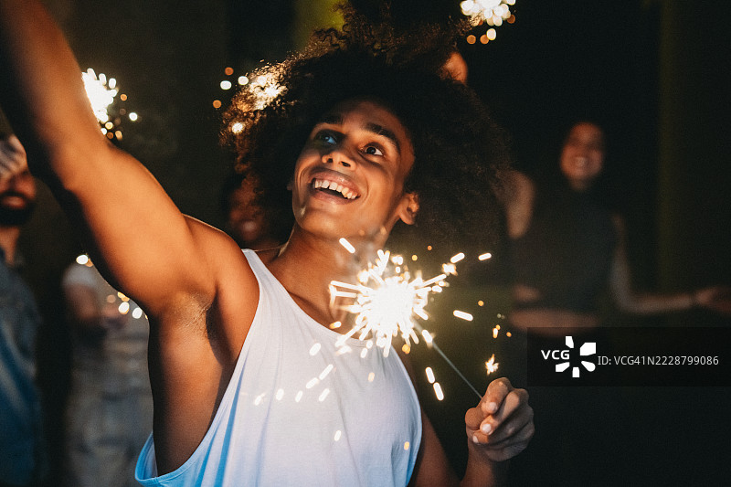 年轻男子在夜晚与朋友们庆祝，挥舞着烟花棒图片素材