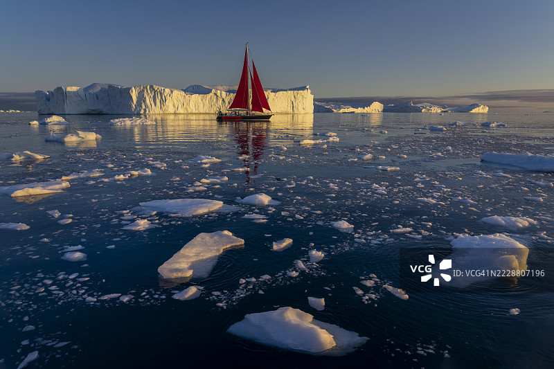 美丽的风景，漂浮的冰山和在夏季午夜阳光下的红色帆船图片素材