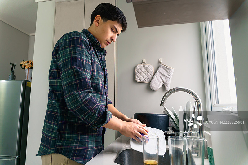 年轻的拉丁裔男子在现代厨房洗碗图片素材