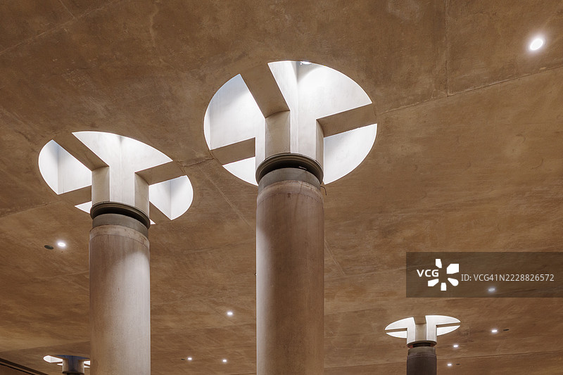 巨大的混凝土柱子支撑着粗糙的混凝土天花板，顶部装有大型圆形天窗，让自然光线透入。图片素材