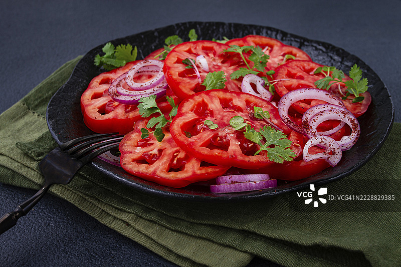 新鲜切片的番茄和红洋葱，配以香草装饰，放在黑色盘子上，夏季沙拉，无人。图片素材