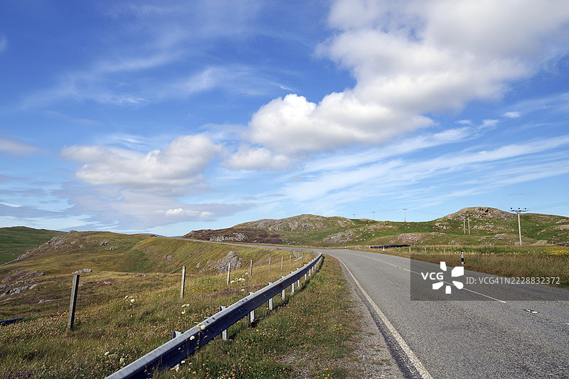 空旷的道路蜿蜒穿过丘陵风景，蓝天上飘着白云，地点：埃尚尼斯，设得兰群岛，苏格兰，英国图片素材