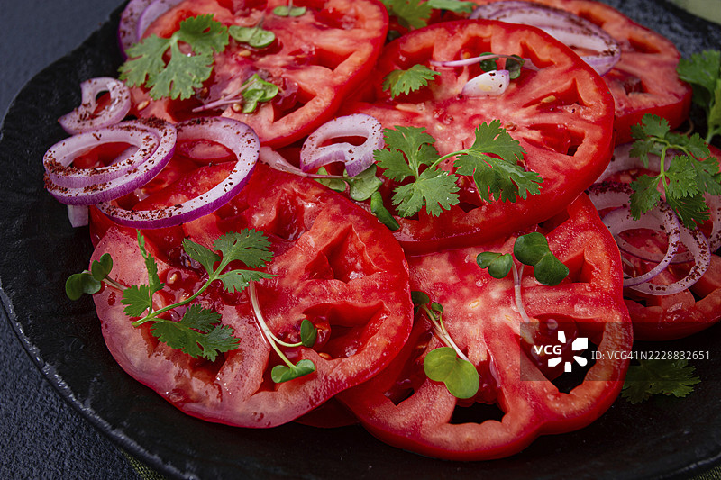 新鲜切片的番茄和红洋葱，配以香草装饰，放在黑色盘子上，夏季沙拉，无人。图片素材