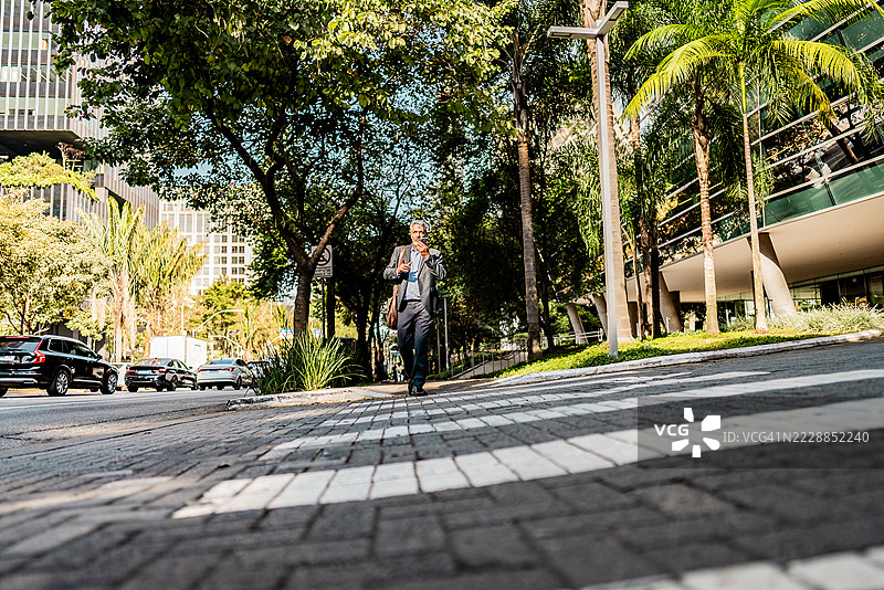 一位高级商人在街上走路时通过手机发送语音信息图片素材