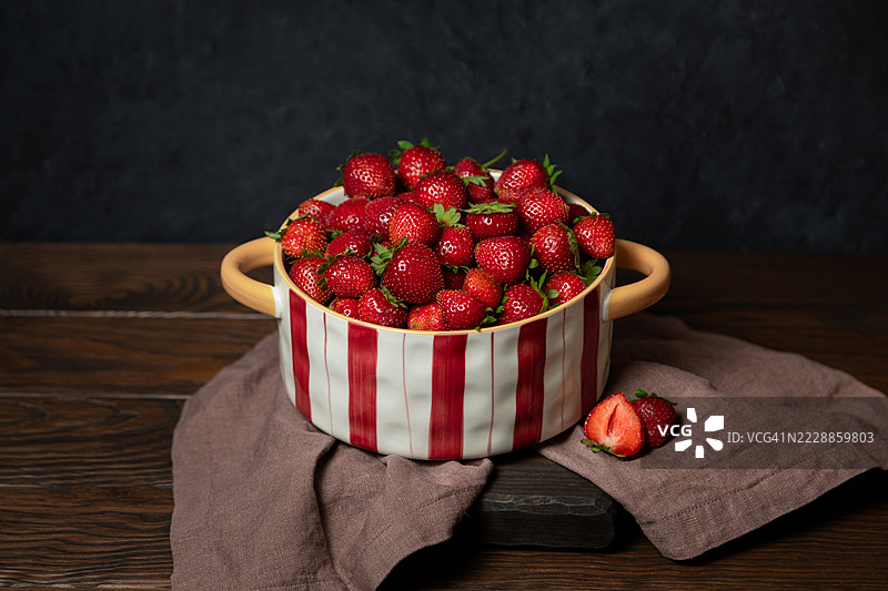 红色条纹碗中的草莓，背景为木质纹理图片素材