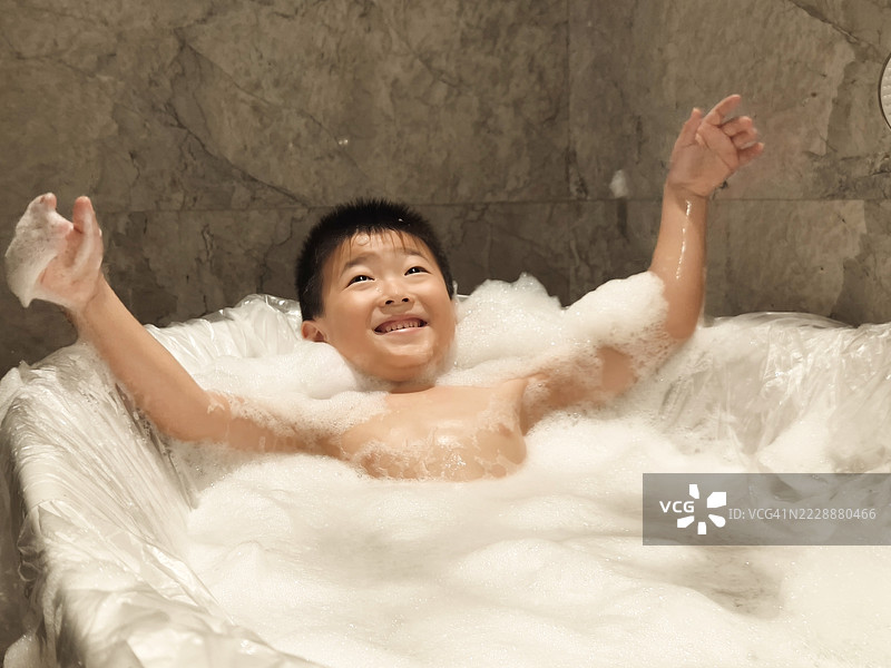 小男孩躺在浴缸里玩泡泡浴。图片素材