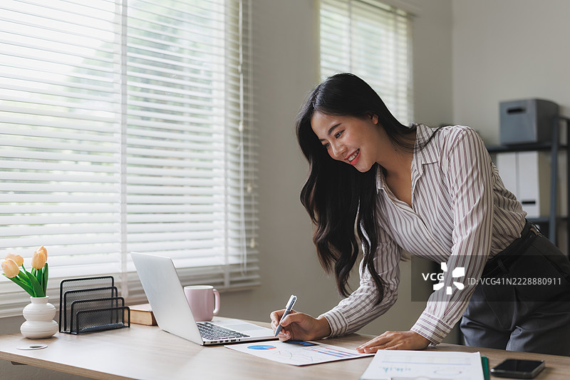 年轻的亚洲女商人在现代办公室分析图表并使用笔记本电脑工作图片素材