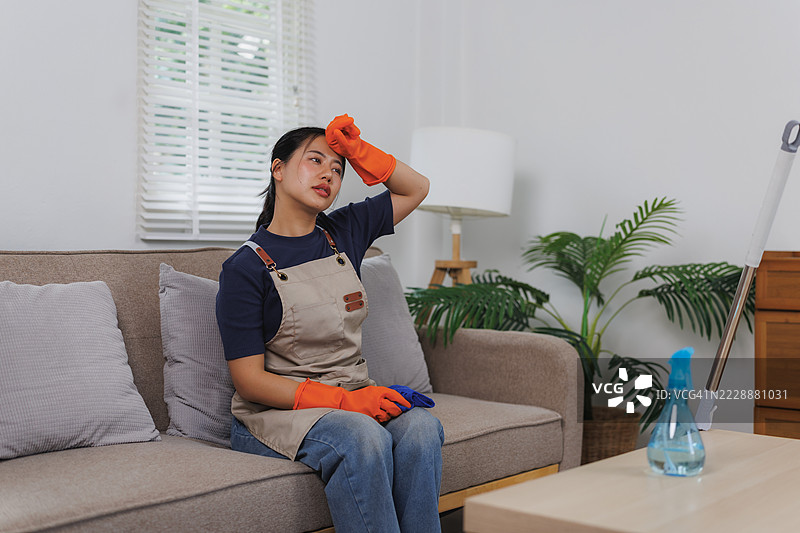 疲惫的亚洲女管家在沙发上休息，刚刚打扫完房子图片素材