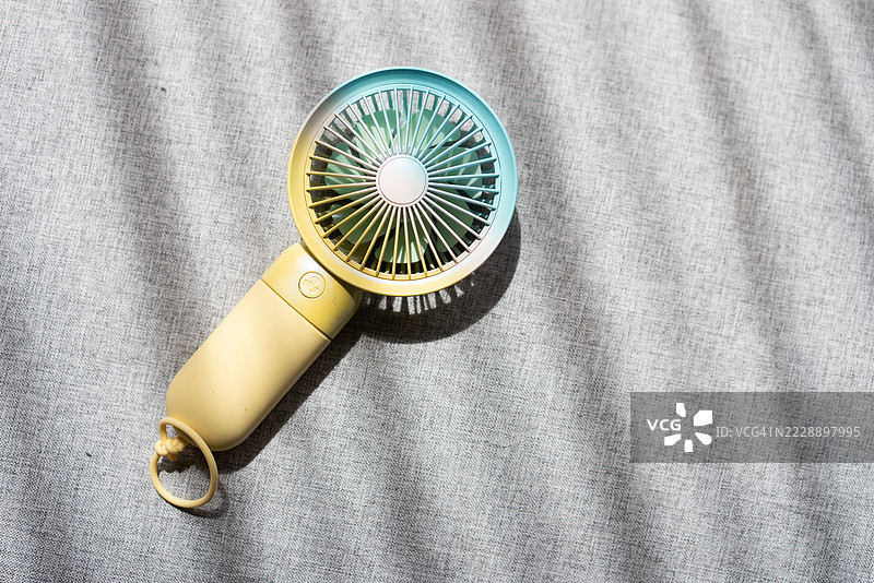 灰色背景和阳光下的手持电动迷你风扇图片素材