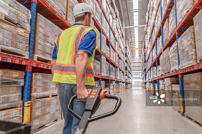 仓库工人使用手动托盘车从货架存储中装载货物，以便运输物流中心。图片素材