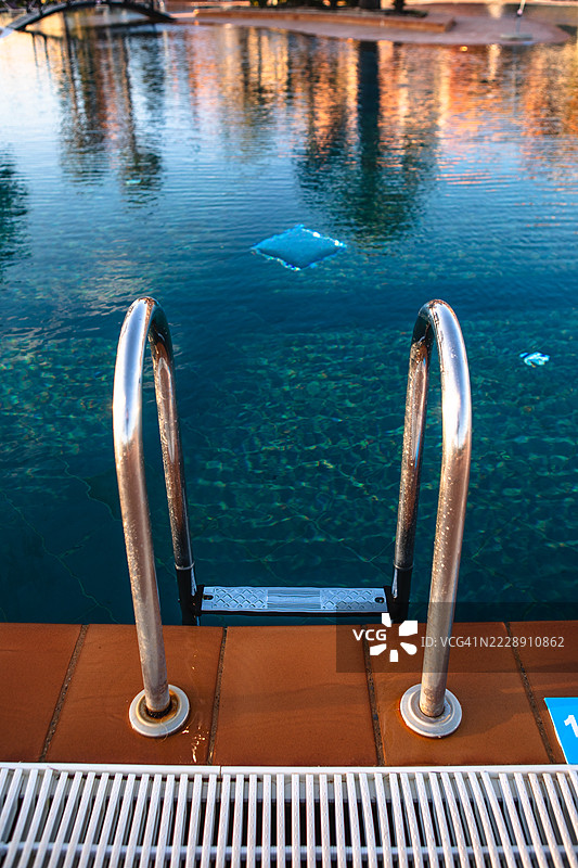 游泳池边缘的瓷砖上反射的泳池梯。图片素材