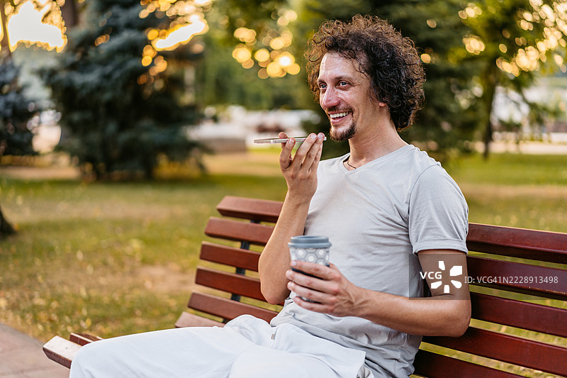 中年男子在公园长椅上喝咖啡时通过手机发送语音消息图片素材
