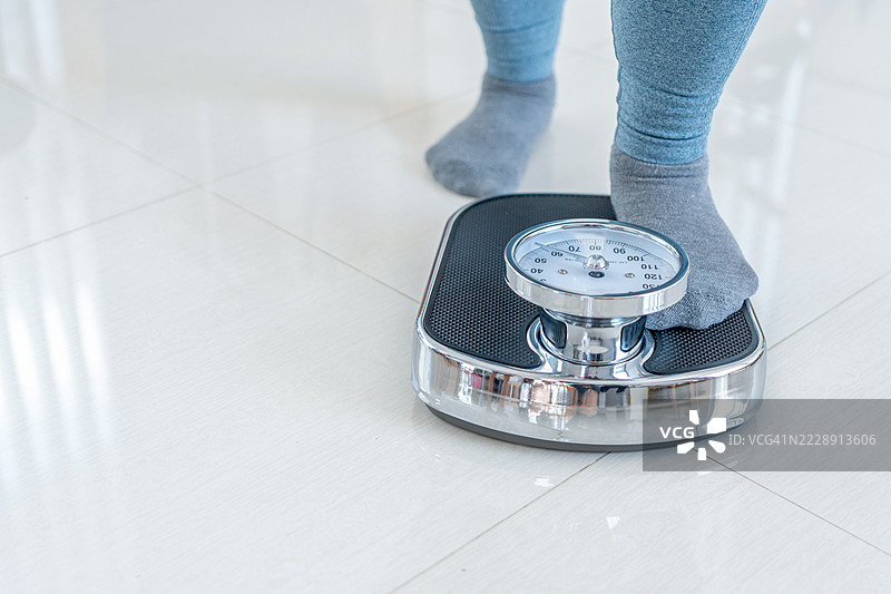 脚踩在秤上。减肥和饮食概念。女性在称重。健身女士在节食。减肥和营养学。黑暗的深夜氛围。图片素材