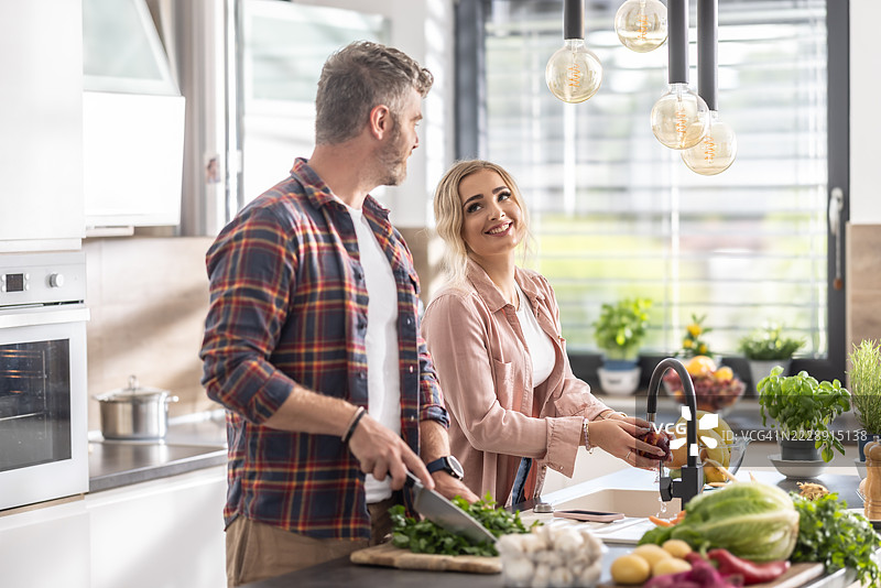 一对年轻情侣在现代厨房里一起准备食物，享受共度时光。图片素材