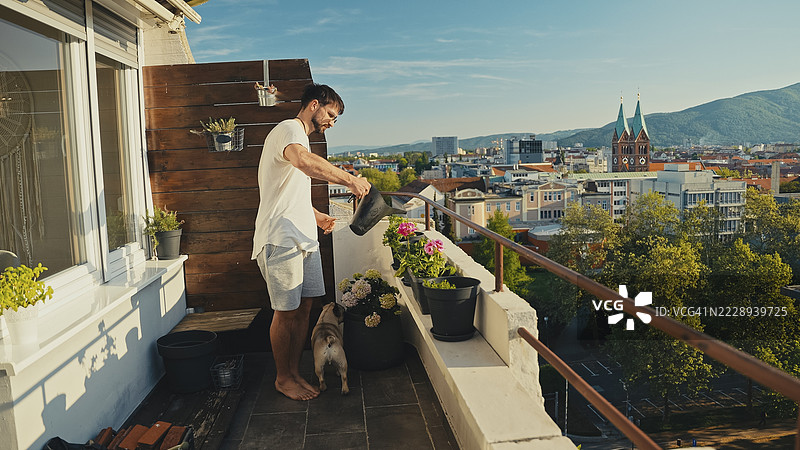 男子在阳台上浇水，俯瞰城市景观图片素材