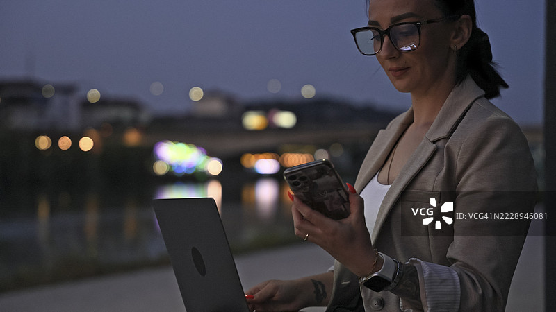 在河边加班的女商人，使用笔记本电脑和智能手机图片素材