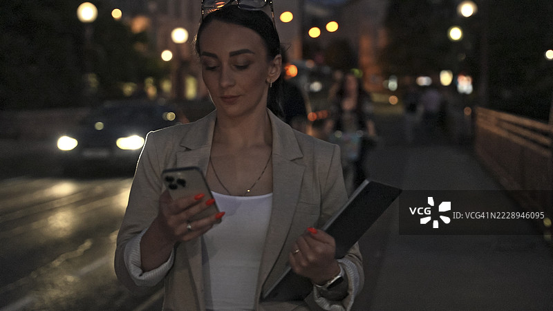 夜晚城市中走路并使用智能手机的女商人图片素材