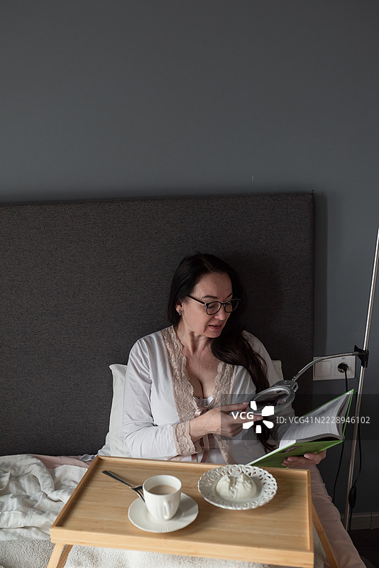 中年女性在床上用放大镜阅读 - 视力与健康概念图片素材