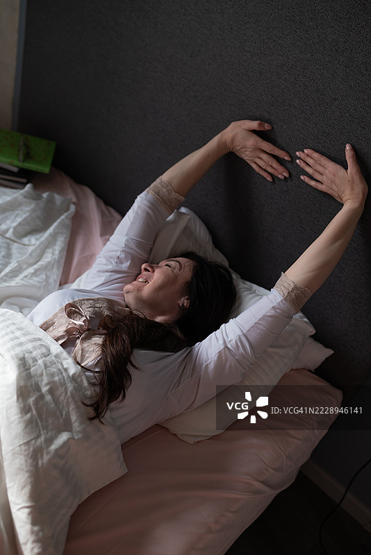 中年女性在床上醒来，伸展身体，开始晨间例行活动图片素材