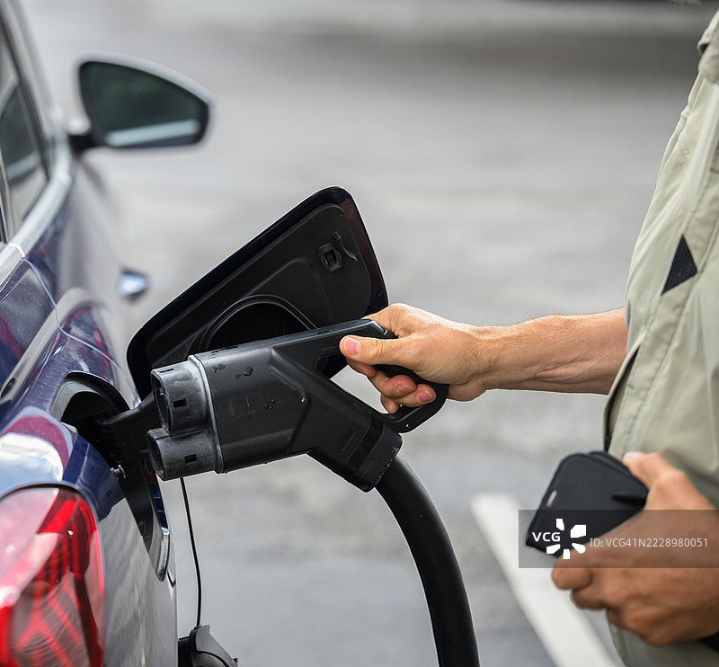 男子正在将电插头连接到电动车上，希望它能开始充电。图片素材