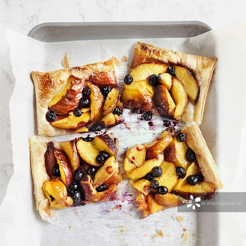 切片桃子和蓝莓的酥皮甜点放在烘焙纸上图片素材