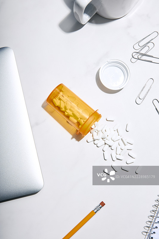 处方瓶中的药丸洒落在桌子上的各种办公用品之间图片素材