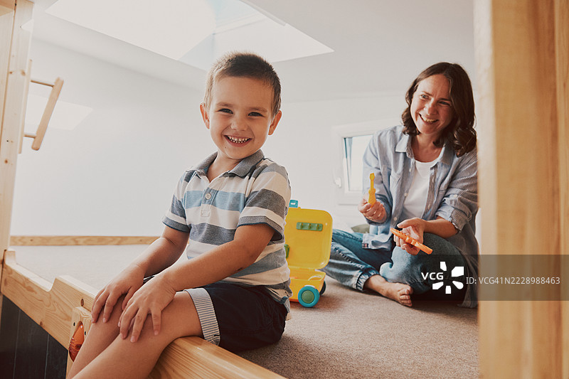 一张母亲和儿子在小房子的狭小空间里坐在床边，玩耍后开心地笑着的照片。图片素材