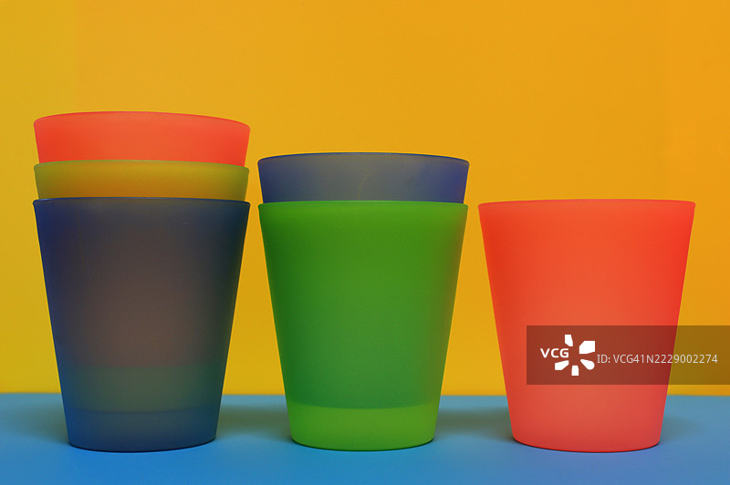 多彩的塑料饮水杯并排堆叠在黄色背景上图片素材