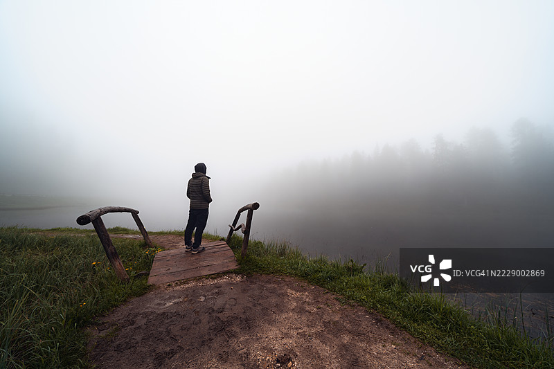 雾气弥漫的湖面上，一座小木桥上的人影。图片素材