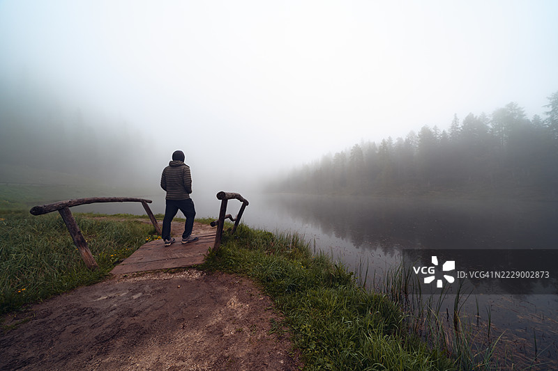 雾气弥漫的湖面上，一个人站在小木桥上的剪影。图片素材