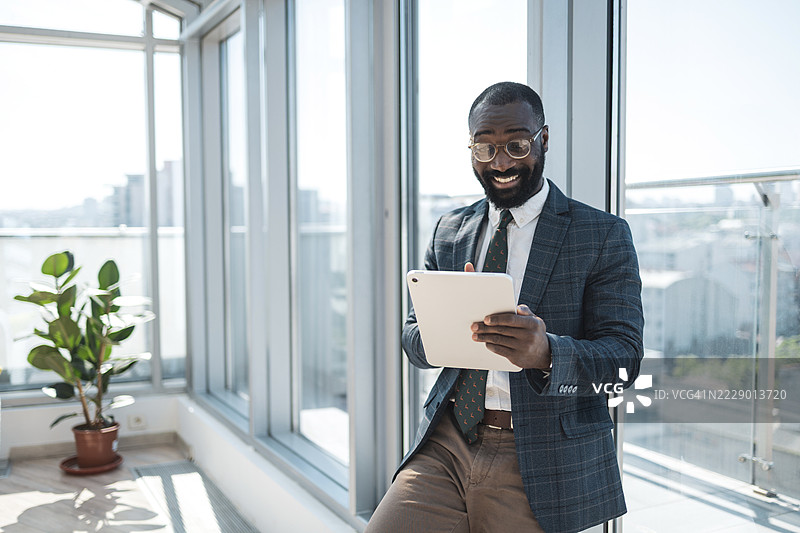 微笑的商人在明亮现代的办公室里使用平板电脑图片素材