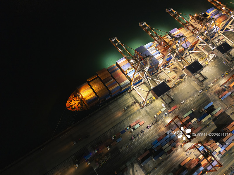 航拍视角下的起重机桥正在商业港口的码头上将集装箱卸载到卡车，适用于商业物流、进出口、运输或货运。图片素材