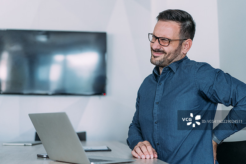 商人在办公室工作时伸展背部。图片素材