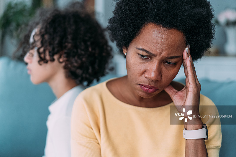 不满的母亲和青少年背靠背坐在家里的沙发上。图片素材