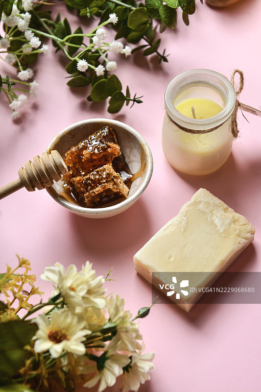 新鲜蜂蜜碗旁边摆放着花朵、手工肥皂和蜡烛图片素材