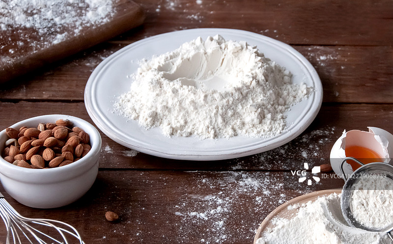 在粗犷的木质表面上摆放的烘焙原料，包括面粉、杏仁和鸡蛋图片素材