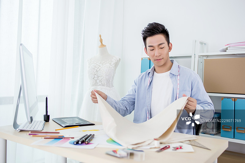 年轻男子正在使用面料和工具进行时尚设计图片素材