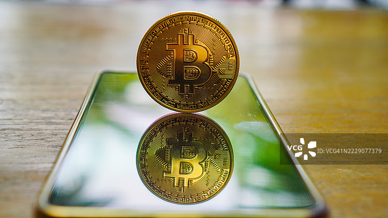 一枚闪亮的实物比特币硬币立在智能手机屏幕上图片素材