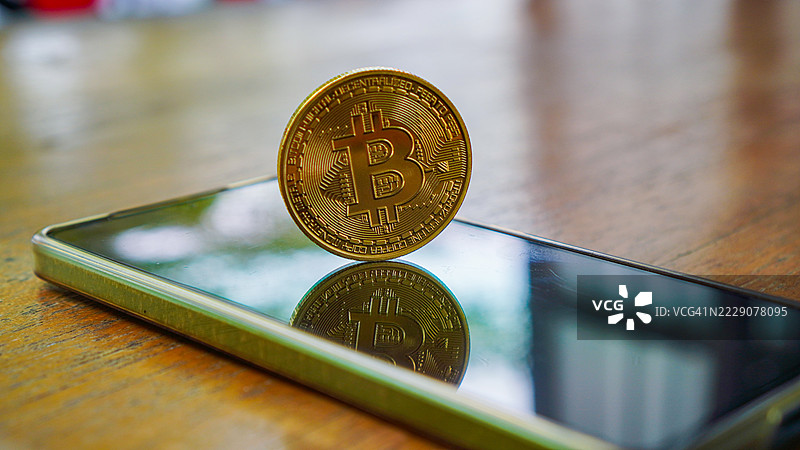 一枚闪亮的实物比特币硬币立在智能手机屏幕上图片素材