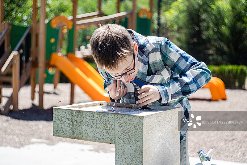 夏季在格鲁吉亚第比利斯公园，青少年男孩在公共饮水喷泉喝水的特写镜头图片素材
