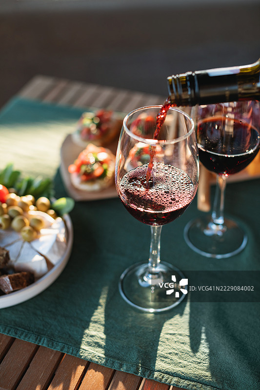 夏天在花园桌上倒入红酒的酒杯旁摆放着各种开胃小吃图片素材
