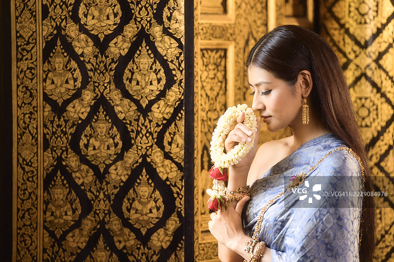 年轻女性身穿传统泰国服饰，侧面特写，闻着花环（Phuang Malai）图片素材