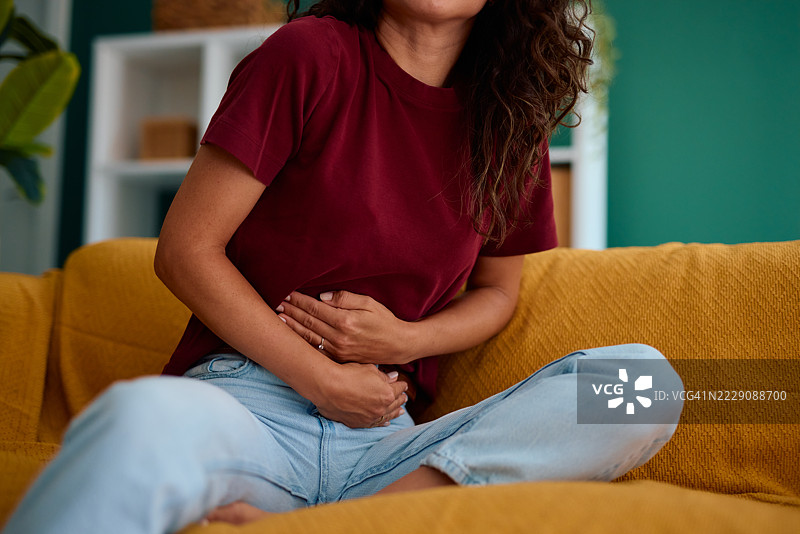 年轻女性在家沙发上坐着，感到腹痛图片素材