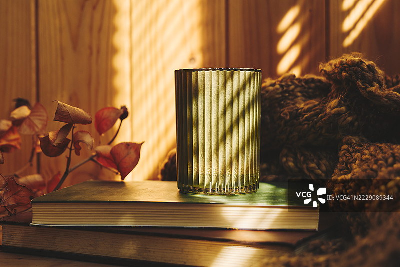 桌子上的绿色蜡烛，旁边是温暖的秋季针织毛衣和书籍。舒适的秋季氛围。图片素材