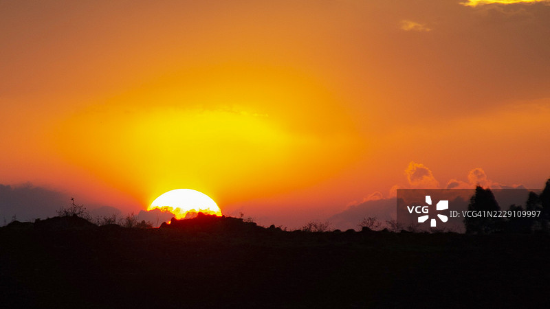 在肯尼亚乌辛吉舒的埃尔多雷特，橙色天空下的树木剪影与田野相映。图片素材