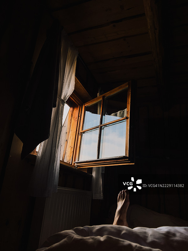 阳光透过开放的窗户洒进温馨的木屋，照亮了床上放松的脚。图片素材