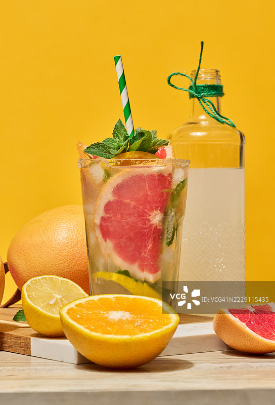 一杯清澈的玻璃杯，装有冷饮，配有葡萄柚片、冰块和薄荷，插着一根绿色条纹的吸管，背景为黄色，乌克兰。图片素材