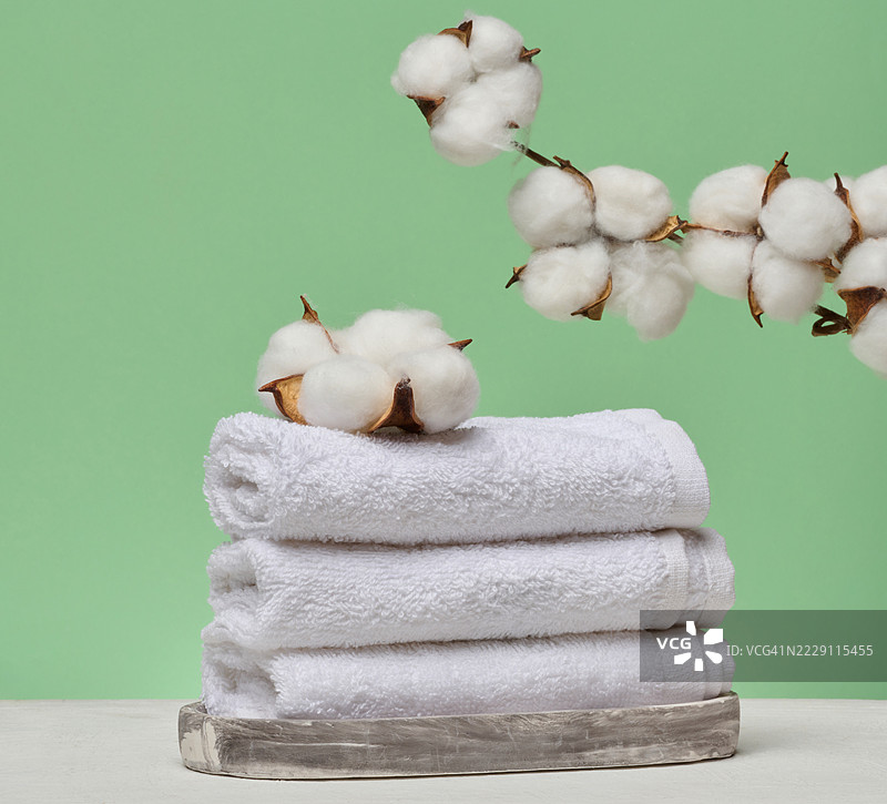 一堆白色折叠毛巾放在大理石台上，上面有天然棉花花序，背景为绿色，乌克兰。图片素材